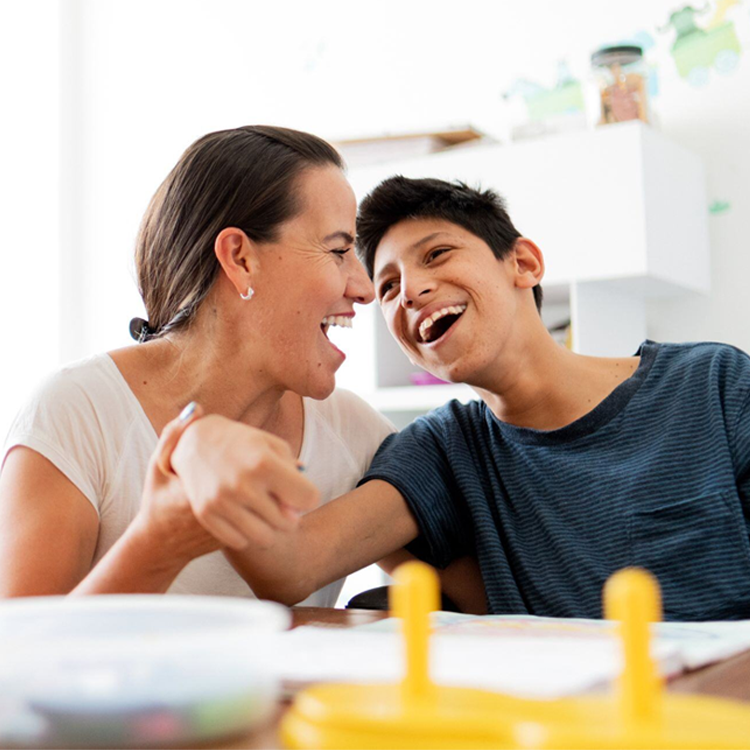 Mamma och son som skrattar tillsammans vid bordet – glädje och samspel i vardagen.