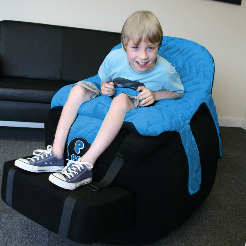 Barn sitter bekvämt i en blå Ppod-stol med fotstöd, leker och ler mot kameran.