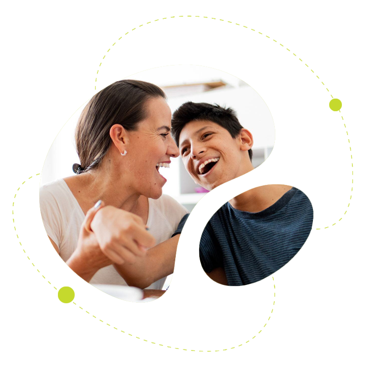 Kvinna och pojke som skrattar tillsammans vid ett bord – symboliserar glädje, delaktighet och trygghet i vardagen.